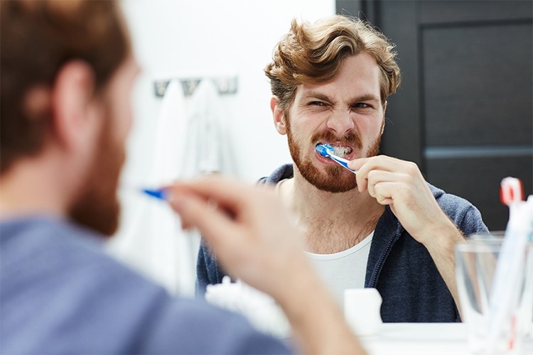 A man brushes his teeth before wearing Invisalign aligners